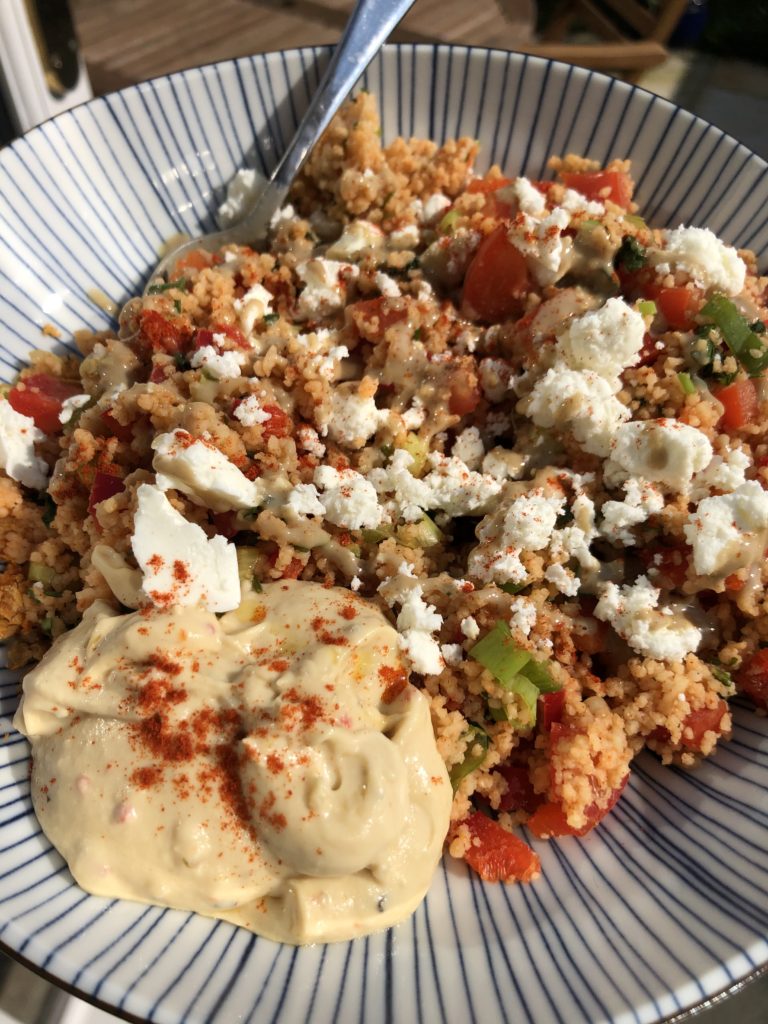 Blue striped bowl with couscous and veggies topped with feta cheese and hummus