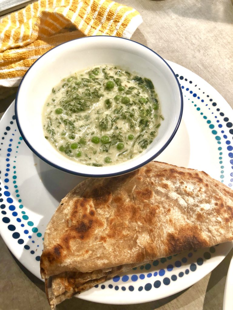 A white curry with fenugreek leaves and peas served on a plate with rotis