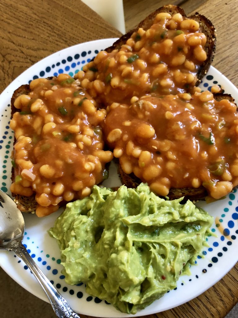 White plate with masala baked beans on toast with smashed avocados