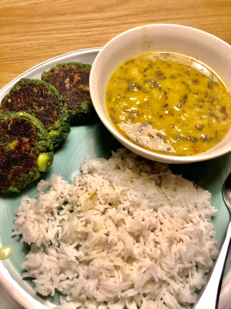 Palak dal served alongside white rice and spinach and potato cutlets on a green dish