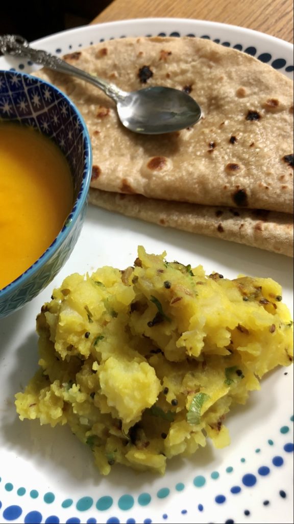 Picnic potatoes with aam was ( mango puree) and rotis on a white plate