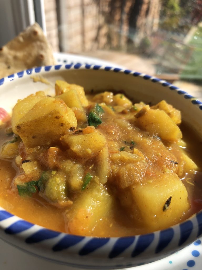 Bowl of curry made with tomatoes, potatoes and peas garnished with coriander leaves