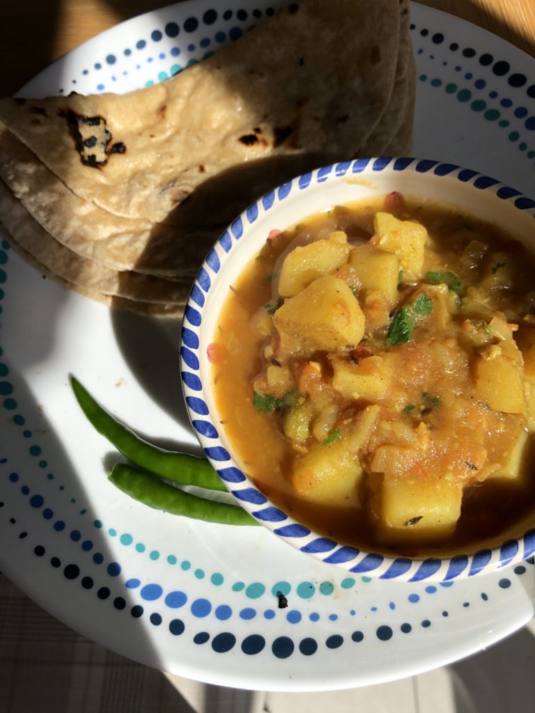 White plate with Indian flatbreads (rotis) and a bowl of aloo mutter - a curry with potatoes, green peas and tomatoes, garnished with coriander leaves