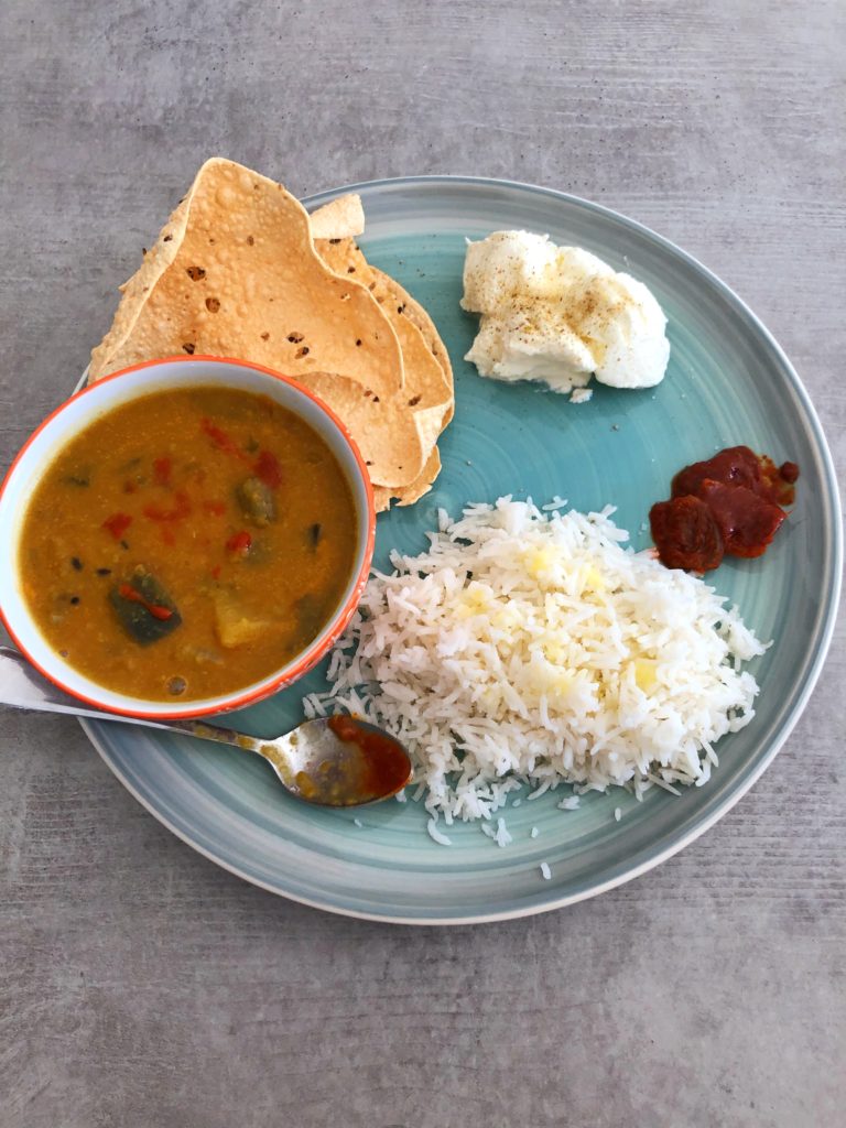 Green dish with sambar - lentil and veggie stew - served alongside rice, poppadoms, yogurt and lemon pickle