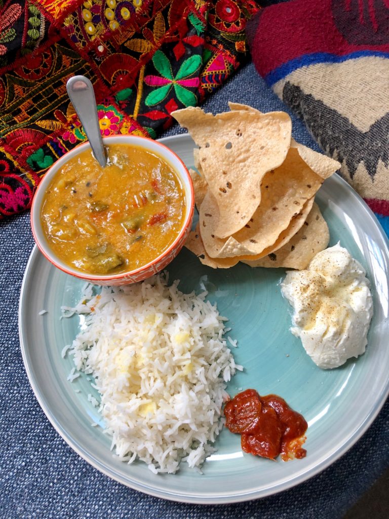 Green dish with sambar - lentil and veggie stew - served alongside rice, poppadoms, yogurt and lemon pickle