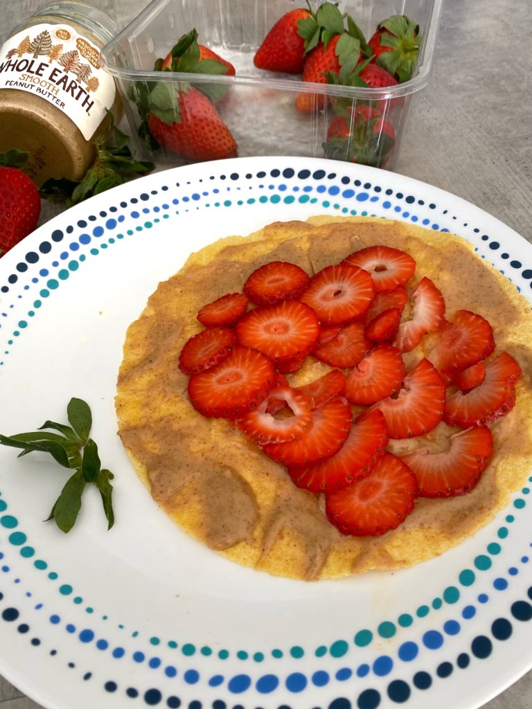 Corn wrap with peanut butter and strawberry slices alongside a peanut butter bottle and a punnet of strawberries