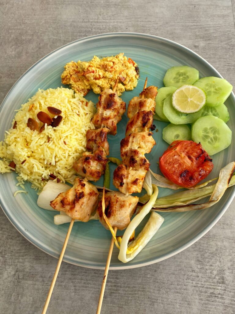 Jujeh kebab or Persian saffron chicken skewers served alongside saffron rice, cucumber slices and grilled tomatoes and spring onions 