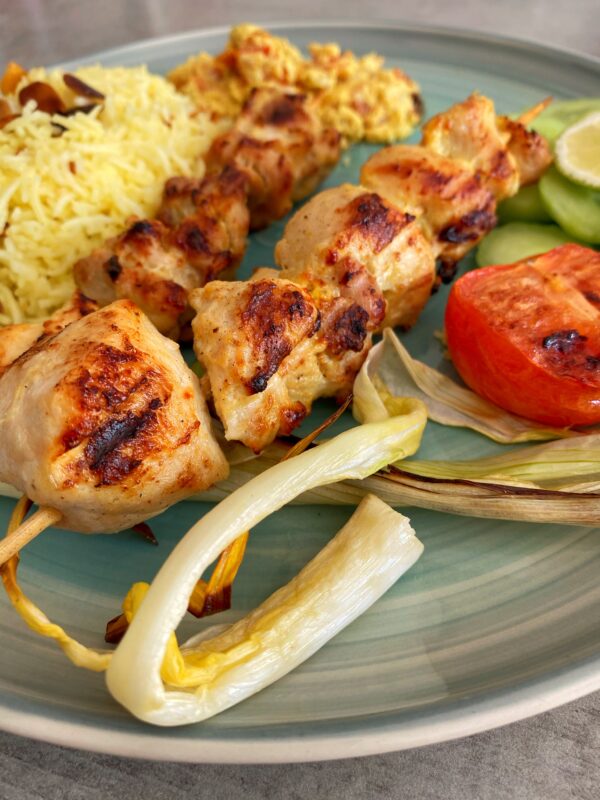 Jujeh kebab or Persian saffron chicken skewers served alongside saffron rice, cucumber slices and grilled tomatoes and spring onions