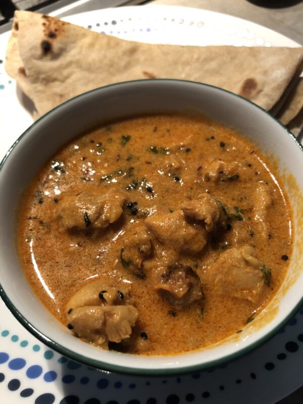 Achari chicken curry - a chicken curry in pickling spice served in a white bowl alongside rotis