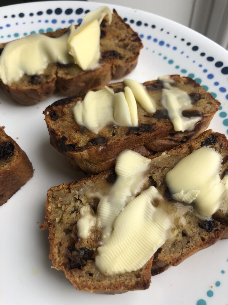 Sugarfree banana bread topped with flaked almonds served with salted butter on a white dish